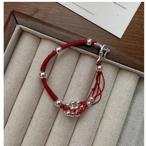 Close-up of red braided rope bracelet with multiple polished silver beads on a beige tray
