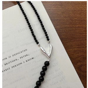 Macro detail of black beaded S925 silver necklace with textured V pendant on book background