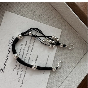 Close-up of black braided cord bracelet with polished silver beads and hook clasp