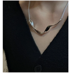 Close-up of a polished S925 sterling silver liquid-style wavy pendant on a black shirt