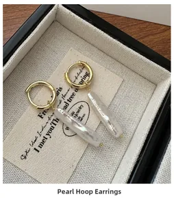 Detailed shot of golden hoop earrings with long baroque pearls in a beige jewelry box