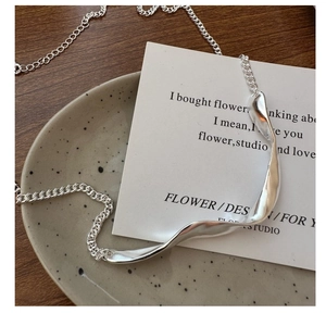 Detailed view of silver wave pendant on a curb chain over a minimalist background