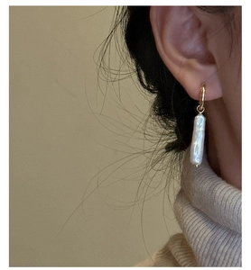 Close-up of a gold hoop earring with a baroque pearl on a woman in a beige sweater