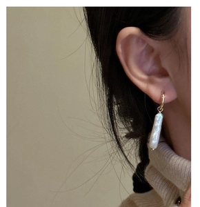 Macro view of gold hoop earring with a long baroque pearl on a model's ear