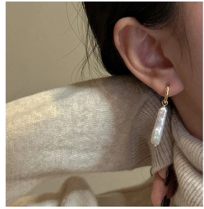Elegant gold hoop earrings with baroque pearl charms worn by a model in lifestyle setting
