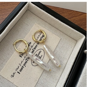 Detail of baroque pearl earrings with golden hoops displayed in a vintage jewelry box