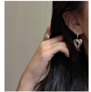 Detailed view of heart-shaped silver earrings with glossy finish on a female model