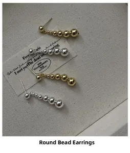 Detail of graduated silver and gold bead earrings displayed on a textured fabric background