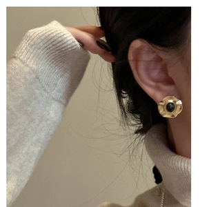 Detail of vintage gold hammered earring with a black stone on a model wearing beige