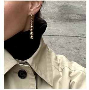 Detail of long gold beaded drop earrings with polished metallic spheres on a model