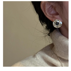 Macro shot of silver hammer-textured stud earring with dark stone on a model in beige knitwear