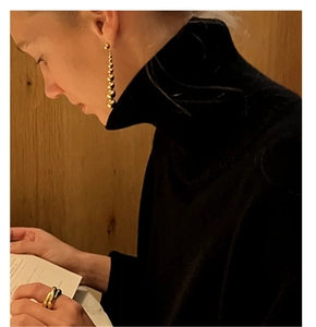 Detail of elegant gold beaded earrings and thick ring set worn on a black turtleneck