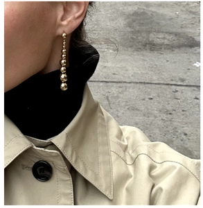 Close-up of golden beaded drop earrings worn by a model in a stylish outdoor setting