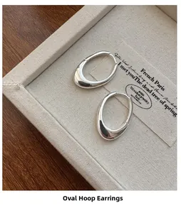 Close-up of minimalist oval S925 sterling silver hoop earrings on a beige fabric tray