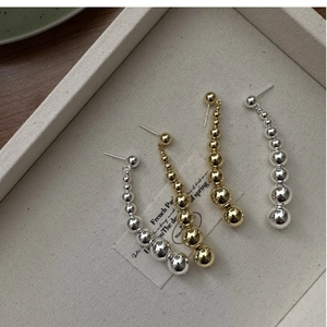 Macro shot of silver and gold gradient beaded earrings on a beige textured tray