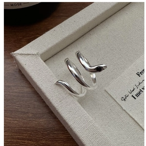Detailed close-up of a silver snake ring with a black gemstone eye on a cream tray