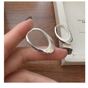 Close-up of polished S925 sterling silver oval hoop earrings held by hand
