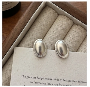 Détail de boucles d'oreilles ovales en argent mat avec bordure texturée sur écrin