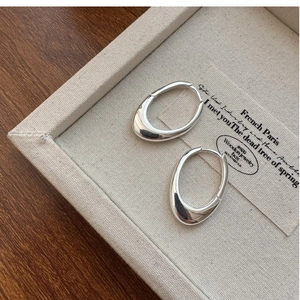 Detailed view of silver oval hoop earrings on a textured jewelry tray with professional lighting