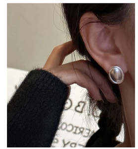 Gros plan de boucles d'oreilles ovales en argent S925 mat portées par un mannequin chic