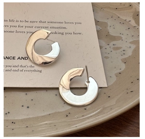 Close-up of polished S925 sterling silver C-shaped hoop earrings on a ceramic dish