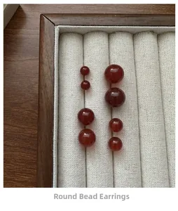 Close-up of smooth round red agate stud earrings in four sizes on a wooden display tray
