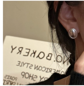 Gros plan de boucles d'oreilles ovales argentées mates portées par un mannequin de style rétro
