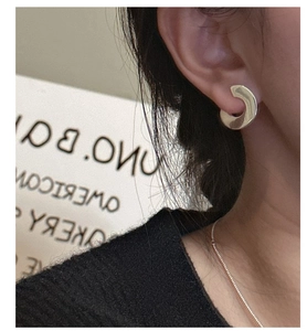 Close-up of minimalist silver C-shaped stud earring worn on ear with a polished metal finish