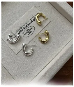 Détail macro de boucles d'oreilles C irrégulières mates en argent et or sur plateau