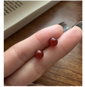 Macro shot of polished S925 sterling silver red agate stud earrings held between fingers
