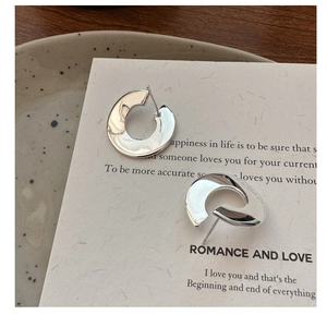 Detail of C-shaped chunky silver earrings with liquid metal texture on a cream card
