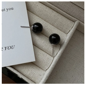 Detail of round black agate stud earrings on a beige fabric jewelry box setting