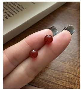 Close-up of red agate bead earrings being held, showing smooth texture and deep red hue