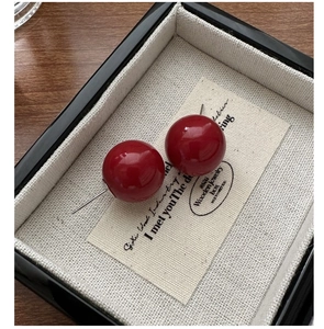 Detailed view of glossy red spherical stud earrings in a luxury gift box