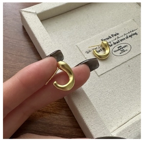 Gros plan de boucles d'oreilles C en argent S925 avec finition dorée mate sur écrin