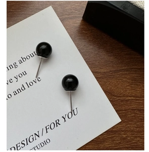 Macro detail of round black onyx stud earrings on a white display card with wood background
