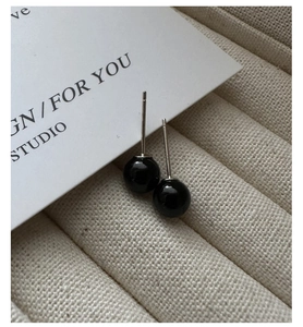 Macro detail of black agate stud earrings on a textured beige tray with silver posts