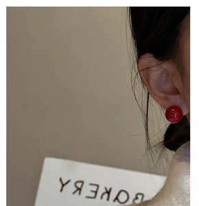 Close-up of minimalist red round stud earrings worn by a model in a clean lifestyle shot