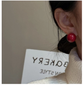 Close-up of a model wearing minimalist red spherical stud earrings with a glossy finish