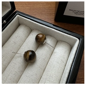 Macro view of S925 silver stud earrings featuring polished tiger eye stone beads