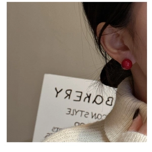 Close-up of a glossy red pearl stud earring on model with elegant holiday vibe