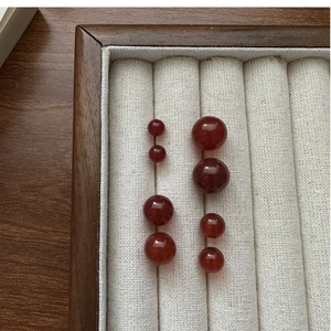 Macro shot of polished red agate beads in various sizes on a wooden jewelry display tray