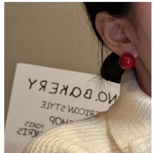 Close-up of red ball stud earrings on model with a cozy white knit sweater background