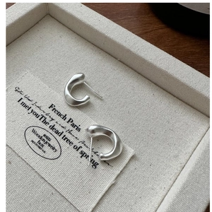 Gros plan de boucles d'oreilles argentées mates en forme de C sur un plateau beige