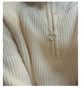 Détail du collier noeud de coeur S925 argenté porté sur un col de pull beige