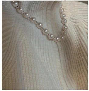 Detail of round white pearl necklace with silver beads on a beige knit sweater
