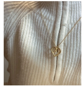 Gros plan d'un collier avec pendentif cœur noué doré sur un pull en maille blanc
