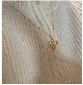 Détail d'un collier doré minimaliste en forme de cœur sur un pull en maille côtelée