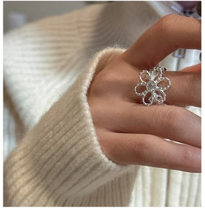 Detailed view of a silver flower ring with zircon stone worn against a soft sweater
