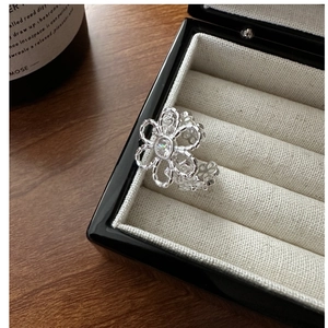 Detailed close-up of hollow flower silver ring with zircon stone and woven band